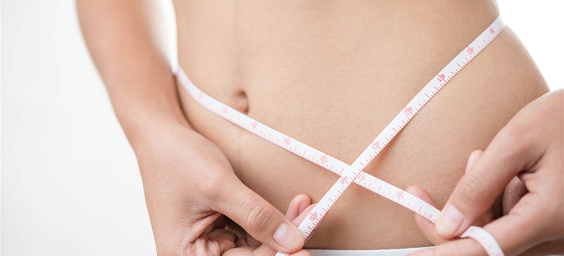 Woman abdomen with measuring tape over grey background.