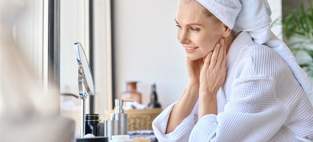 woman applying skincare products in her bath towel at her vanity